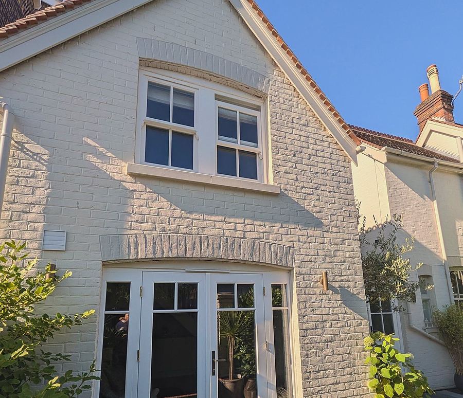 A painted brick annex in Reigate with a timber sash window above and glazed French doors below