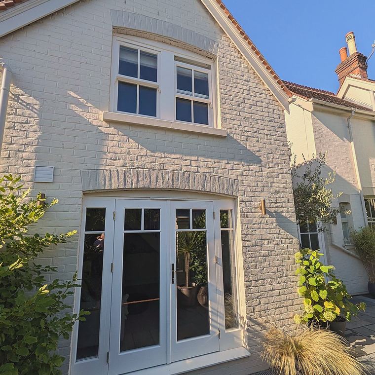 Gable elevation of a painted brick annex in Reigate with a Georgian sash window above and glazed timber French doors below
