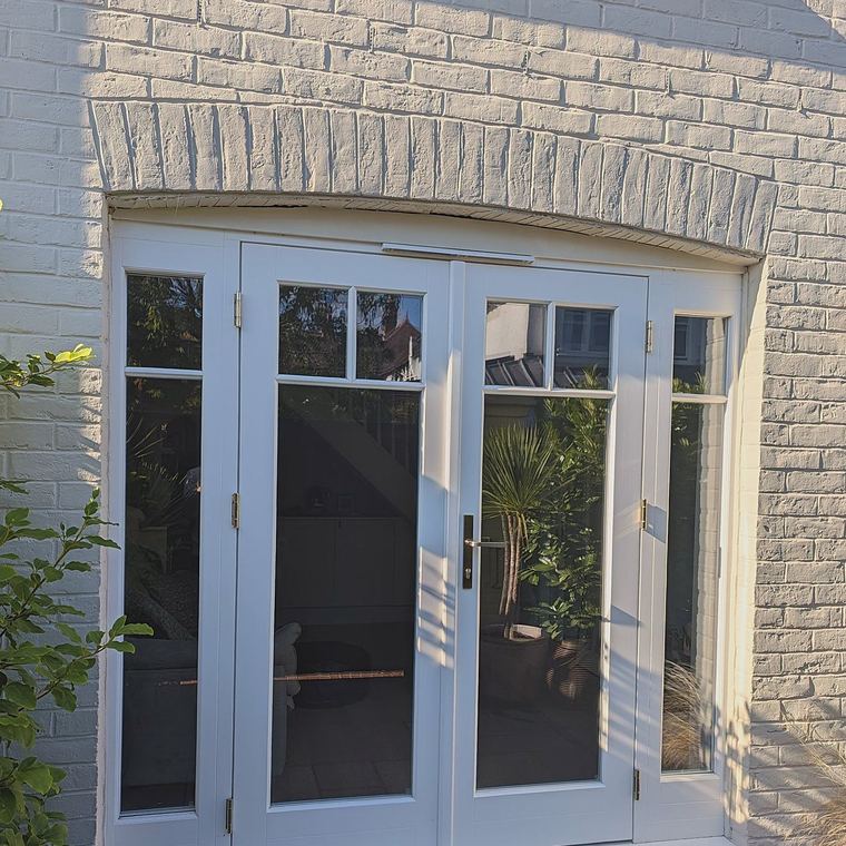 Timber French doors with glazing bars and full height sidelights, set under a gauged brick arch