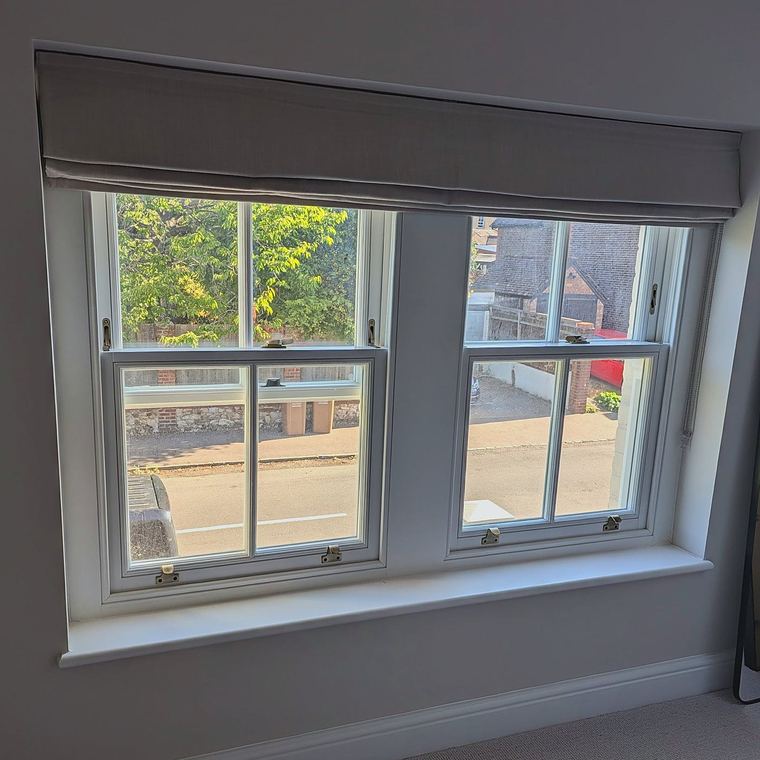 A pair of timber sash windows seen from inside a bedroom, with brass fasteners and sash lifts