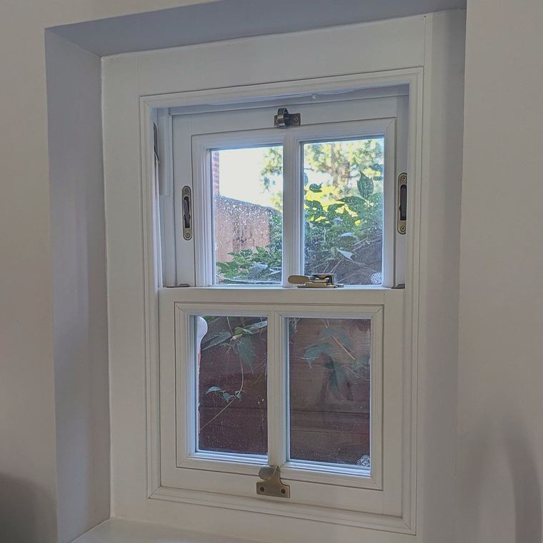 A timber sash window above a kitchen worktop with the upper sash slid down for ventilation